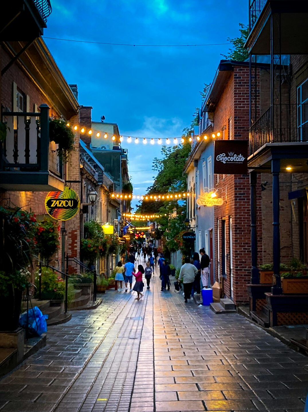 Colorful Chilean neighborhood street at dusk with string lights and pedestrians